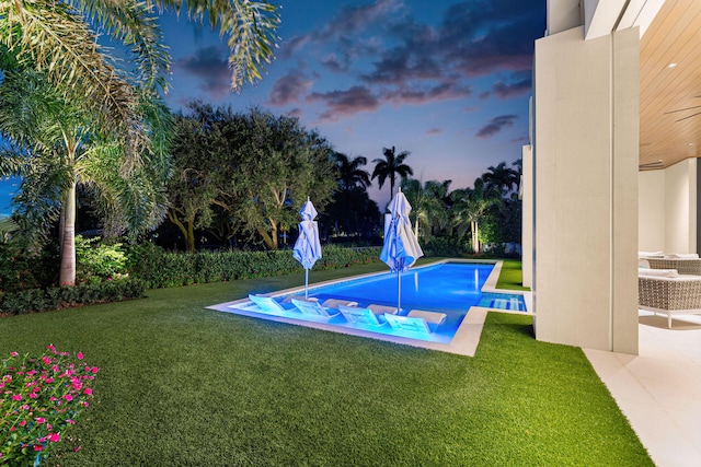 pool at dusk with a patio, a hot tub, and a lawn