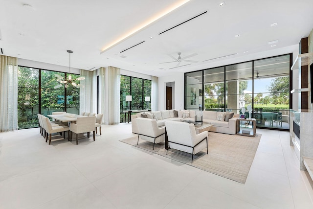 living room featuring ceiling fan with notable chandelier, a wall of windows, and light tile patterned floors