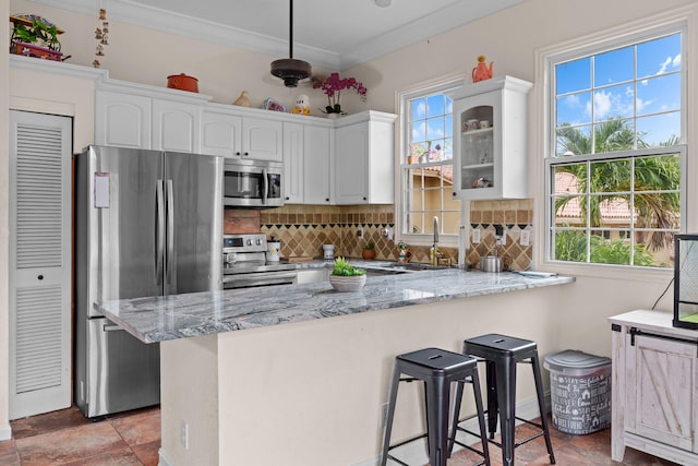 kitchen featuring white cabinetry, a kitchen breakfast bar, light stone counters, kitchen peninsula, and appliances with stainless steel finishes