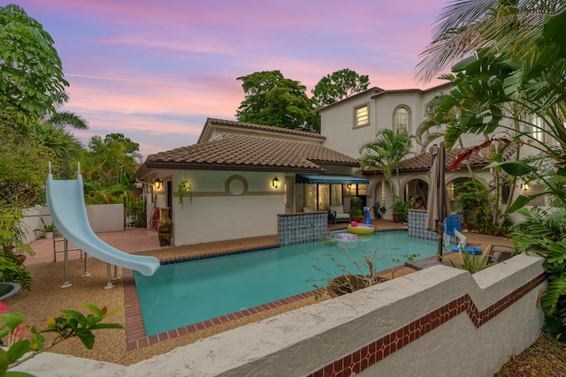 pool at dusk with a water slide and a patio