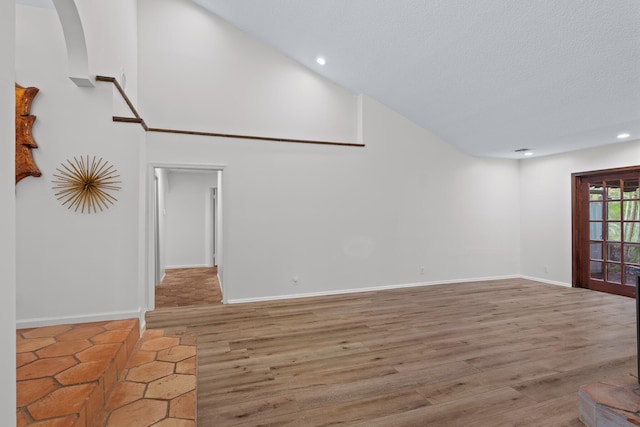 unfurnished room with a textured ceiling, a towering ceiling, and hardwood / wood-style flooring