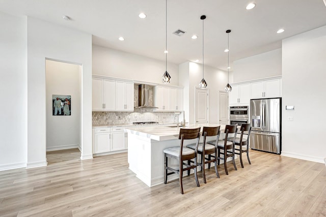 kitchen featuring a center island with sink, stainless steel appliances, light wood-type flooring, and white cabinets