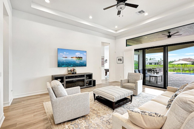 living room with light hardwood / wood-style flooring, ceiling fan, and a tray ceiling