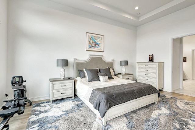 bedroom with light wood-type flooring, a high ceiling, a tray ceiling, and ceiling fan