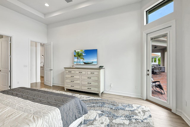 bedroom featuring a raised ceiling, a high ceiling, wood-type flooring, access to outside, and ceiling fan