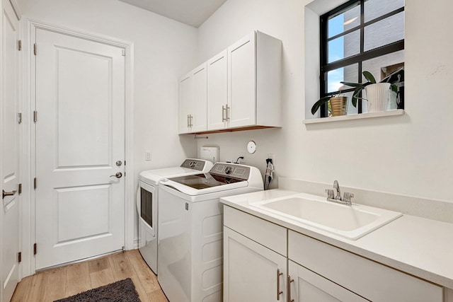 laundry area with sink, light hardwood / wood-style floors, cabinets, and washing machine and dryer