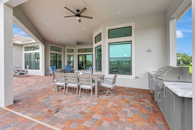 patio terrace at dusk with grilling area, an outdoor kitchen, sink, and ceiling fan