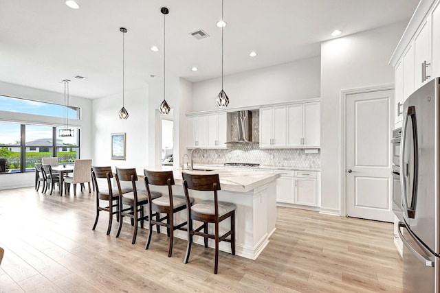 kitchen with white cabinets, decorative light fixtures, light wood-type flooring, appliances with stainless steel finishes, and wall chimney range hood