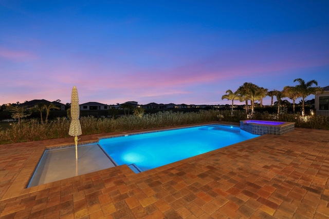 pool at dusk with a patio area and an in ground hot tub