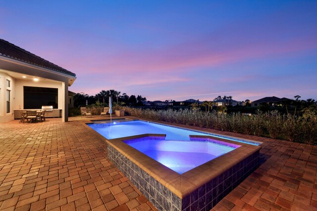 pool at dusk featuring a patio and an in ground hot tub