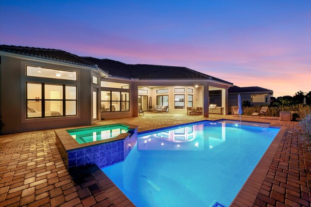 pool at dusk with a patio and an in ground hot tub