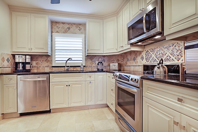 kitchen featuring sink, dark stone countertops, stainless steel appliances, cream cabinets, and decorative backsplash