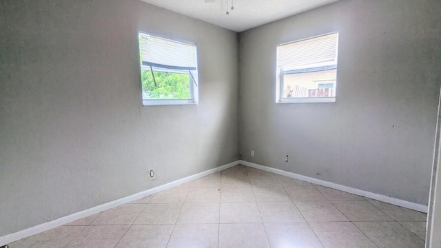 unfurnished room with light tile patterned flooring, a textured ceiling, and baseboards