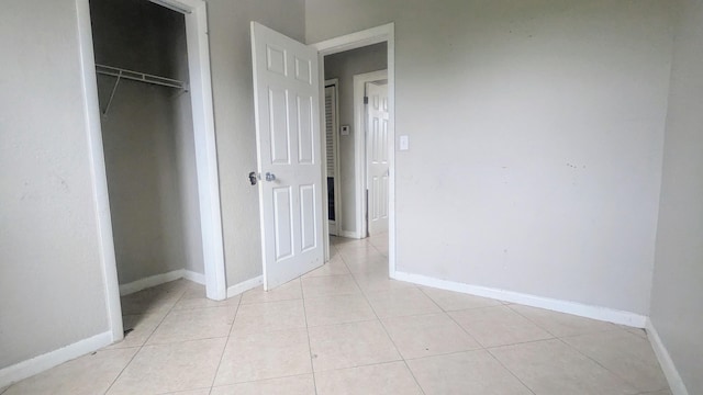 unfurnished bedroom featuring light tile patterned floors, baseboards, and a closet