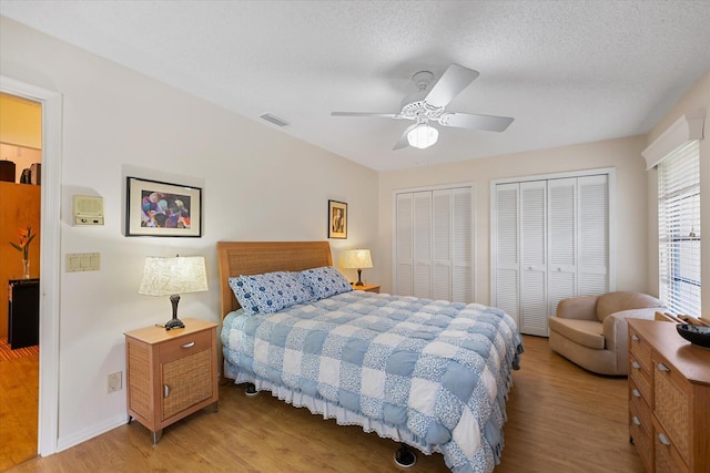 bedroom featuring a textured ceiling, two closets, light hardwood / wood-style flooring, and ceiling fan