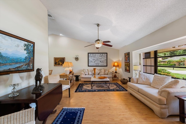 living room with a textured ceiling, light hardwood / wood-style floors, vaulted ceiling, and ceiling fan