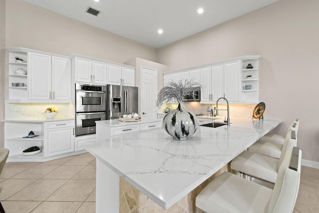 kitchen featuring stainless steel appliances, light stone counters, white cabinets, a kitchen bar, and kitchen peninsula