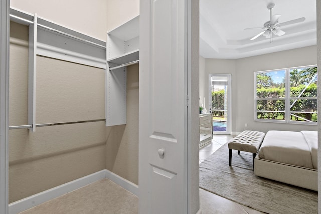 spacious closet featuring ceiling fan, a tray ceiling, and light tile patterned floors