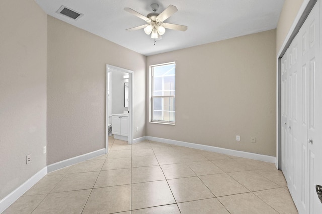 unfurnished bedroom with connected bathroom, light tile patterned floors, a closet, and ceiling fan