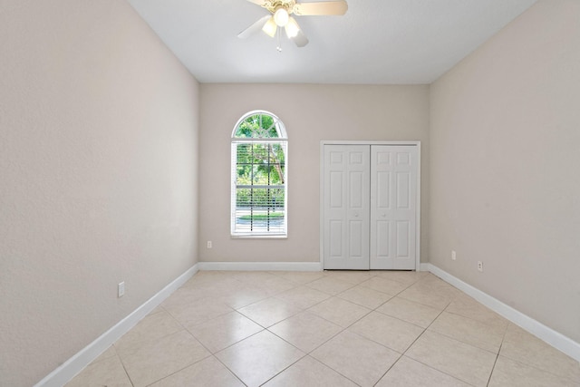 unfurnished bedroom with light tile patterned flooring, ceiling fan, and a closet