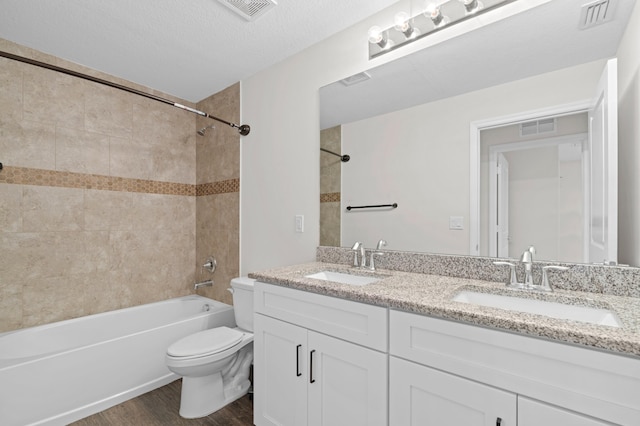 full bathroom featuring vanity, a textured ceiling, tiled shower / bath, toilet, and hardwood / wood-style flooring