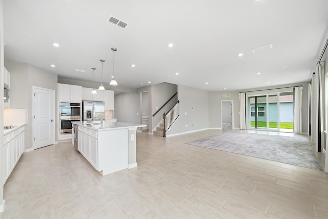 kitchen with stainless steel appliances, backsplash, decorative light fixtures, a kitchen island with sink, and white cabinets