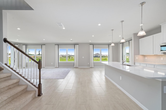 kitchen with white cabinetry, sink, hanging light fixtures, tasteful backsplash, and a center island with sink