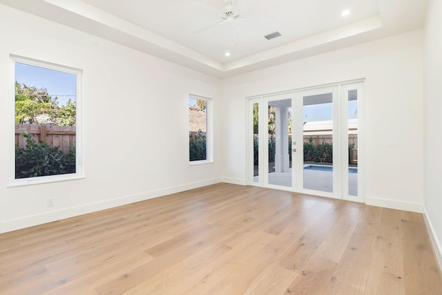 empty room featuring light hardwood / wood-style floors, a raised ceiling, a wealth of natural light, and ceiling fan