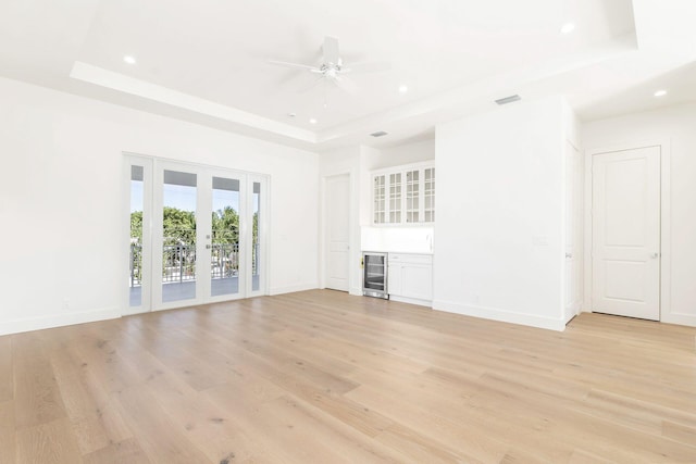 unfurnished living room with a raised ceiling, beverage cooler, and light hardwood / wood-style flooring