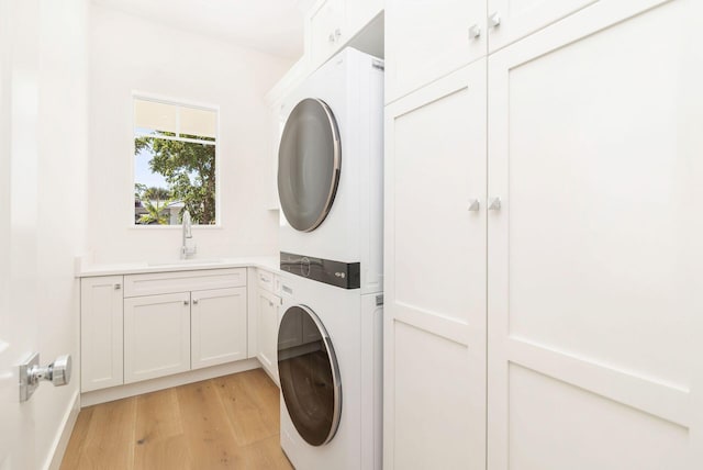 clothes washing area featuring sink, cabinets, light wood-type flooring, and stacked washer / dryer