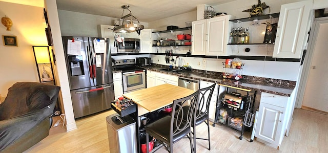 kitchen with decorative light fixtures, appliances with stainless steel finishes, light hardwood / wood-style floors, and white cabinetry