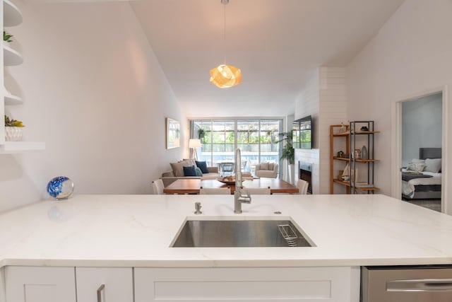 kitchen featuring sink, vaulted ceiling, hanging light fixtures, light stone countertops, and white cabinets