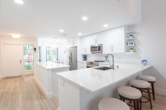 kitchen with sink, a center island, a breakfast bar, appliances with stainless steel finishes, and light hardwood / wood-style flooring