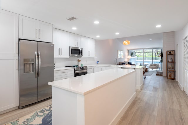 kitchen with white cabinets, sink, light hardwood / wood-style floors, appliances with stainless steel finishes, and kitchen peninsula