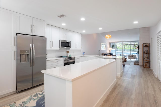 kitchen with sink, appliances with stainless steel finishes, white cabinets, kitchen peninsula, and light wood-type flooring