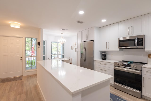 kitchen with white cabinets, a kitchen island, light hardwood / wood-style floors, appliances with stainless steel finishes, and decorative light fixtures