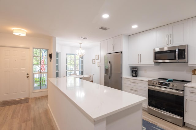 kitchen featuring decorative light fixtures, light wood-type flooring, appliances with stainless steel finishes, a kitchen island, and white cabinets