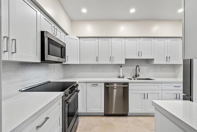 kitchen with stainless steel appliances, white cabinetry, light countertops, and a sink