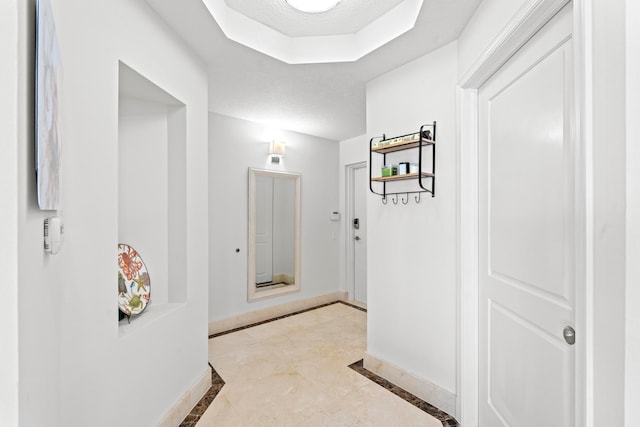 corridor with light tile patterned flooring and a raised ceiling