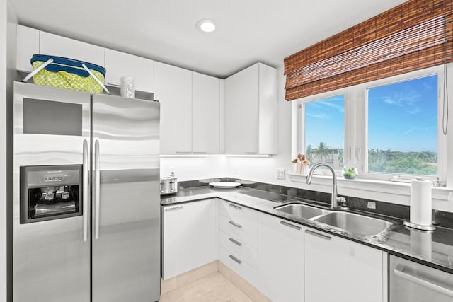 kitchen featuring light tile patterned floors, white cabinets, dark stone counters, appliances with stainless steel finishes, and sink