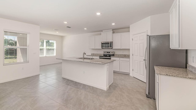 kitchen with light stone countertops, sink, stainless steel appliances, a kitchen island with sink, and white cabinets