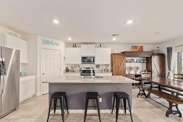 kitchen with white cabinets, sink, a barn door, an island with sink, and appliances with stainless steel finishes