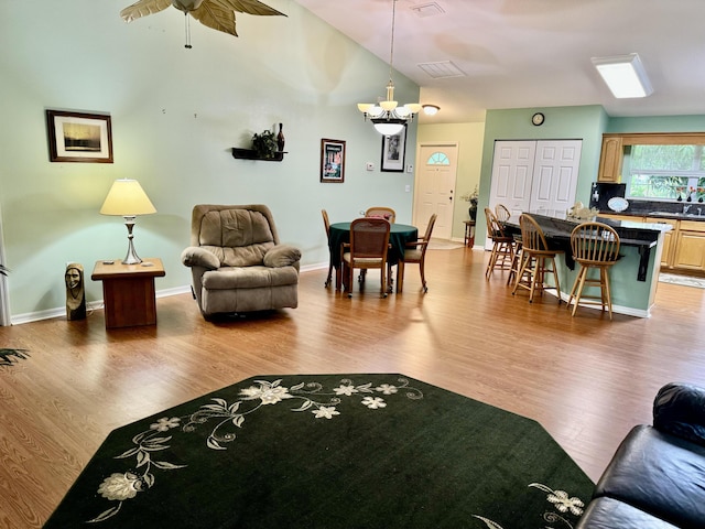 living room with ceiling fan with notable chandelier, high vaulted ceiling, and wood-type flooring