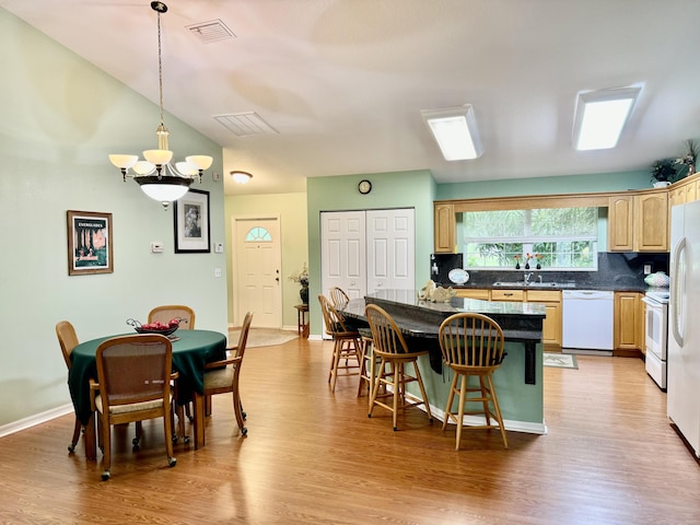 kitchen with hardwood / wood-style flooring, hanging light fixtures, a breakfast bar area, white appliances, and a kitchen island