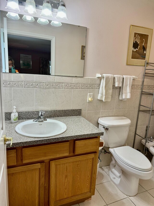 bathroom with tile patterned floors, toilet, tile walls, vanity, and a bidet