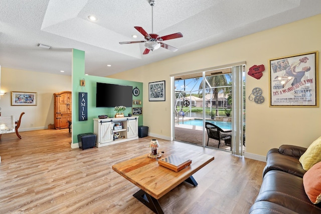 living room with wood-type flooring, a raised ceiling, a textured ceiling, and ceiling fan