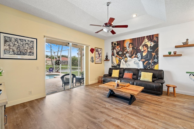 living room with a textured ceiling, wood-type flooring, ceiling fan, and a raised ceiling