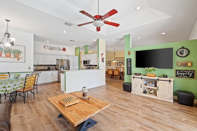 living room featuring light hardwood / wood-style flooring, ceiling fan with notable chandelier, and a tray ceiling