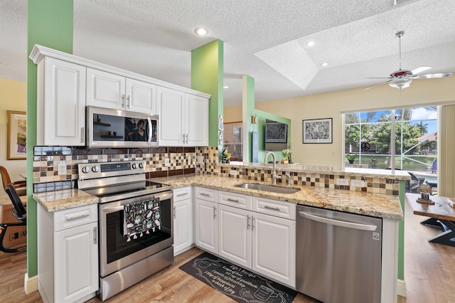 kitchen with sink, appliances with stainless steel finishes, kitchen peninsula, and light hardwood / wood-style floors