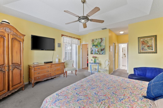 carpeted bedroom featuring a textured ceiling, a raised ceiling, ensuite bathroom, and ceiling fan